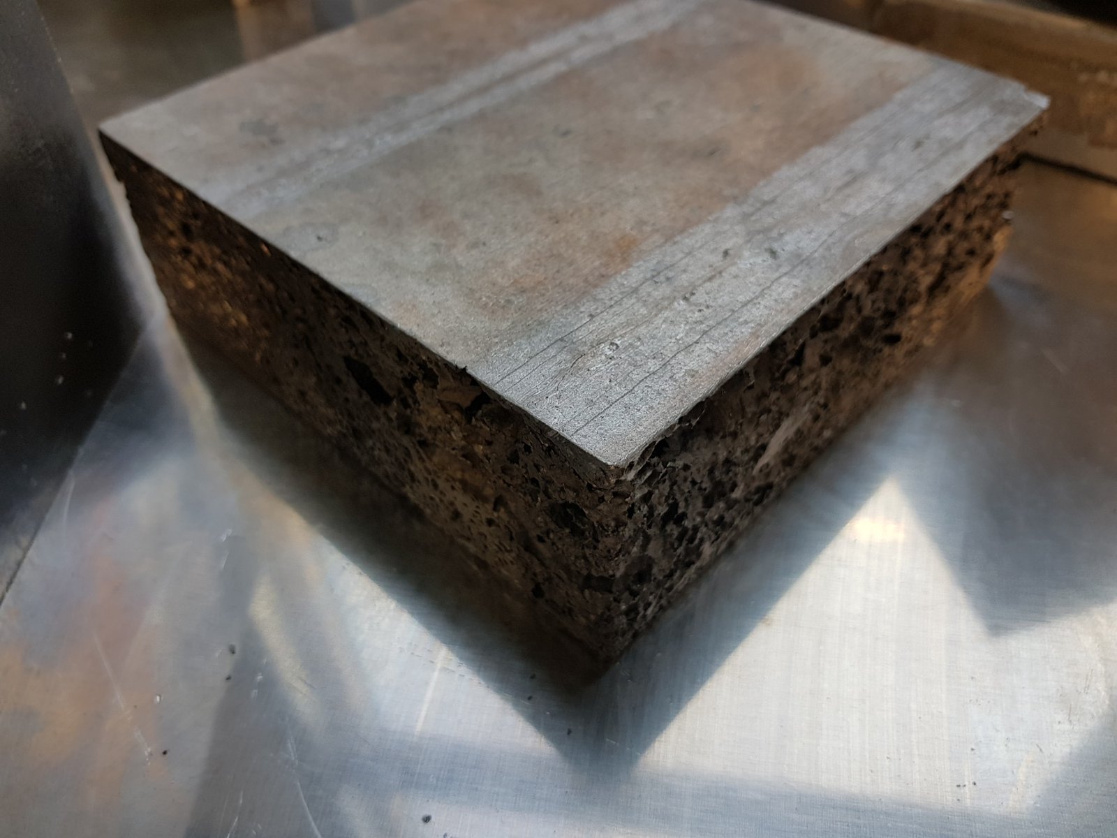 Ein Block Aluminiumschaum auf einer Blechunterlage: Die Oberseite ist eine geschlossene, glatte Gusshaut, nur an den bearbeiteten Seitenflächen sind die Poren zu sehen.